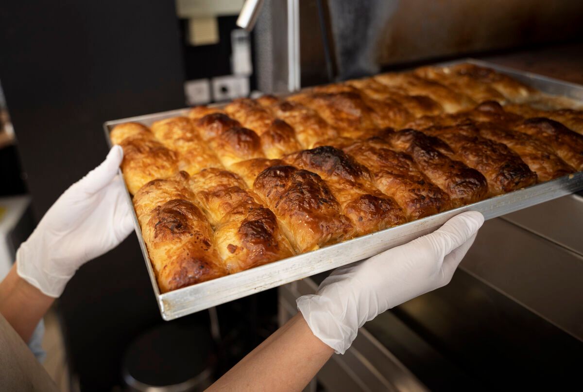 Bandeja de bollería laminada horneada sostenida con guantes en una planta de producción