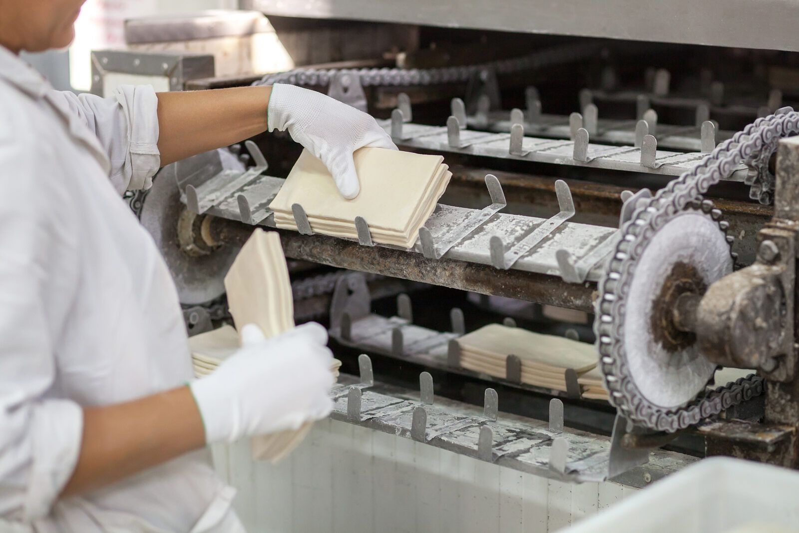 Operaria con guantes manipulando láminas de masa en una línea industrial de semielaborados