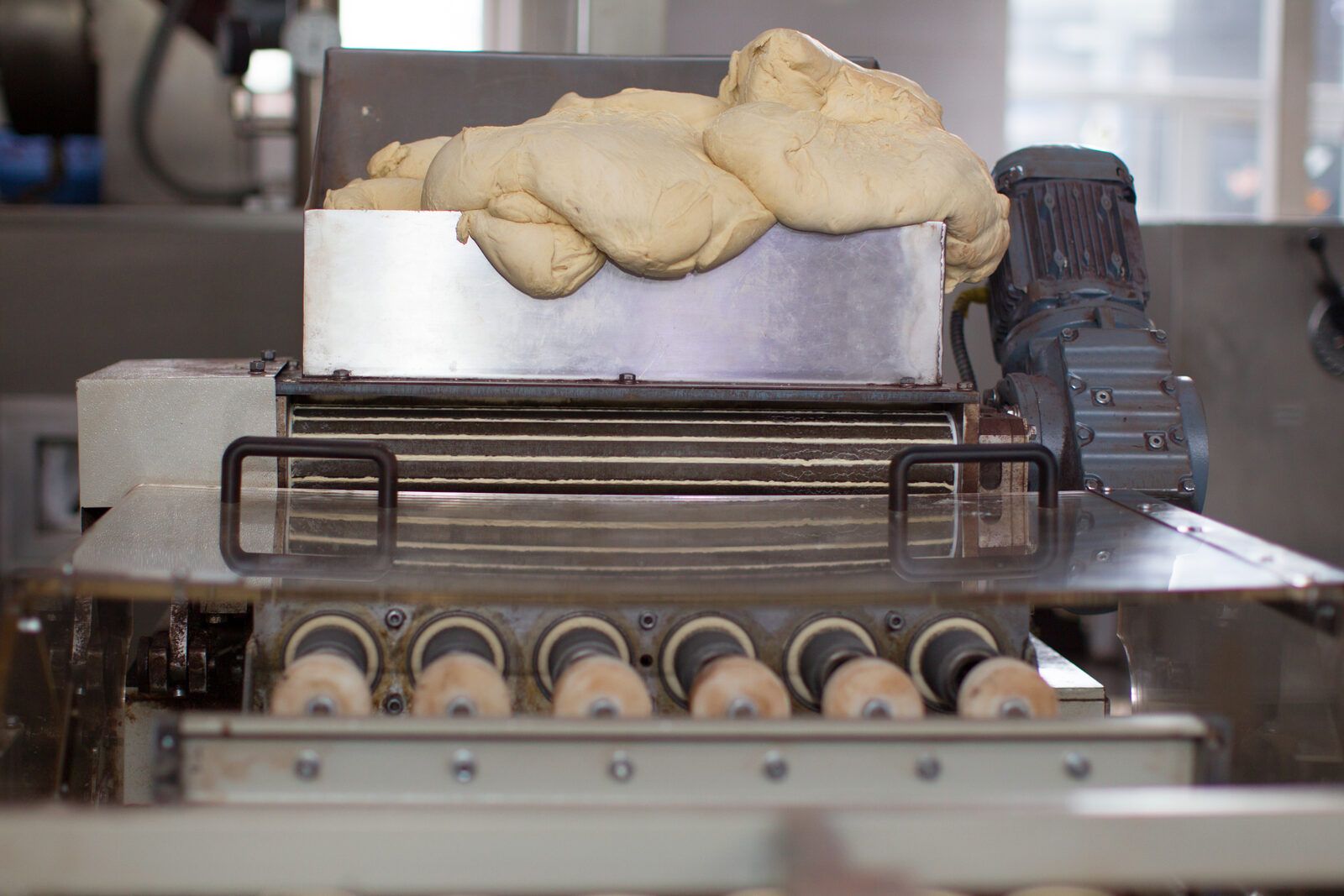 Tolva de alimentación con masa fermentada sobre la cinta de una línea industrial de bollería